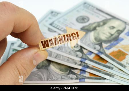 Geschäfts- und Finanzkonzept. In den Händen eines Mannes ist ein Pfeil mit der Inschrift - WARNUNG, im Hintergrund sind Dollars. Stockfoto