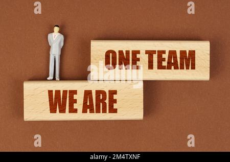 Geschäftskonzept. Auf einer braunen Oberfläche auf Holzblöcken mit der Inschrift "We Are One Team" steht eine Miniaturfigur eines Geschäftsmannes. Stockfoto