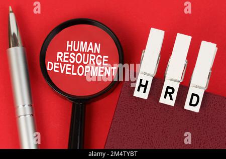 Geschäftskonzept. Auf der roten Oberfläche liegt ein Stift, ein Notizbuch mit Wäschespins - HRD - und eine Lupe mit der Inschrift - Human Resource devel Stockfoto