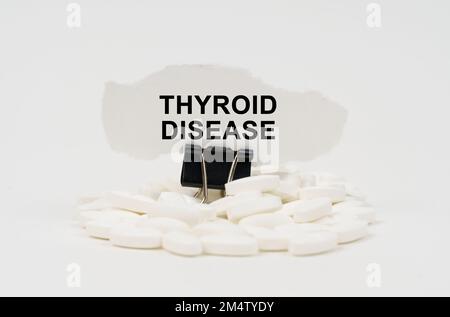 Medizinisches Konzept. Auf einer weißen Oberfläche sind Pillen und zerrissenes Papier mit der Inschrift - Schilddrüsenerkrankung Stockfoto