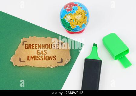 Ökologisches und industrielles Konzept. Auf dem Tisch befinden sich ein Globus und ein Marker, auf grünem Hintergrund befindet sich ein Pappkarton mit der Aufschrift „Greenhouse“ Stockfoto