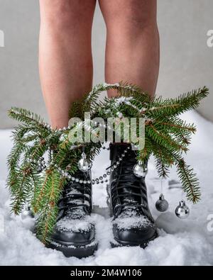 Die Beine einer Person stehen auf Schnee in schweren Stiefeln mit Weihnachtsbaumzweigen Stockfoto