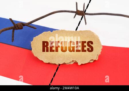 Politisches Konzept. Auf den Flaggen Polens und Russlands liegt ein Pappteller mit der Inschrift "Flüchtlinge". Durch Stacheldraht getrennte Flaggen Stockfoto