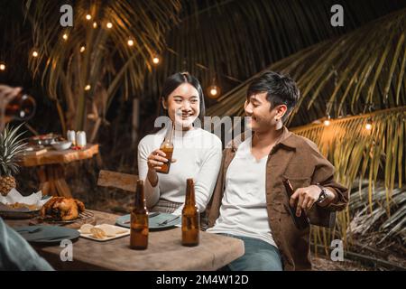 Ein junges asiatisches Paar, das auf einer Gartenparty mit Bier anstoßen will Stockfoto