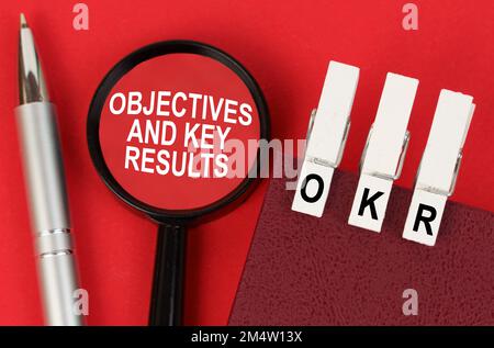 Geschäftskonzept. Auf der roten Oberfläche liegen ein Stift, ein Notizbuch mit Kleiderstücken - OKR - und eine Lupe mit der Beschriftung - Objektive und Schlüssel R. Stockfoto