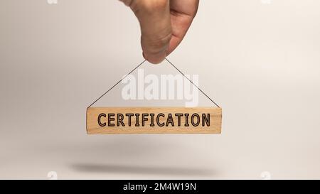Zertifizierungswort. Geschrieben auf einem Holzschild, das in menschlicher Hand hängt Stockfoto