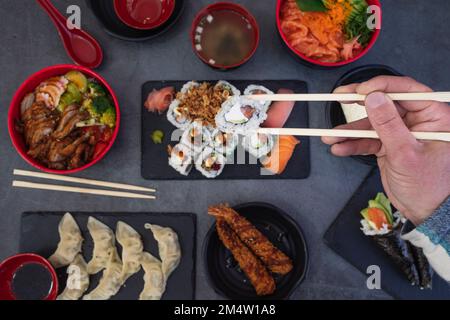 Blick auf die Hände von Männern, die Sushi im japanischen Restaurant essen. Großer Blickwinkel auf Sushi-Hände mit Essstäbchen auf dem Tisch Stockfoto