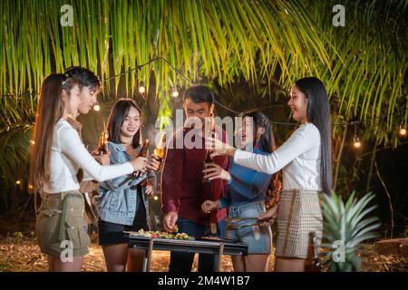 Eine Gruppe asiatischer Freunde, die Spaß beim Grillen im Garten haben und Bier trinken. Stockfoto