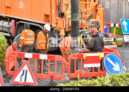 Nahaufnahme von gut sichtbaren Gaslieferanten, die Asphalt für den Fahrer einer Maschine mit Saugbagger aufbrechen, um den flexiblen Bodensaugschlauch UK zu positionieren Stockfoto