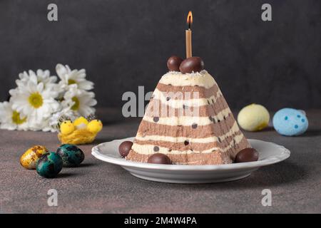 Traditionelles Oster-Hüttenkäse-Dessert mit Schokolade sowie farbenfrohe Eier auf dunkelgrauem Hintergrund Stockfoto