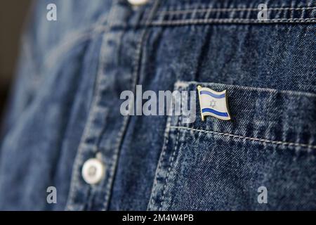 Ein Metallabzeichen mit der Flagge Israels ist auf einer blauen Jeans-Jacke befestigt. Das israelische Patriotismuskonzept. Unabhängigkeitstag in Israel. Stockfoto