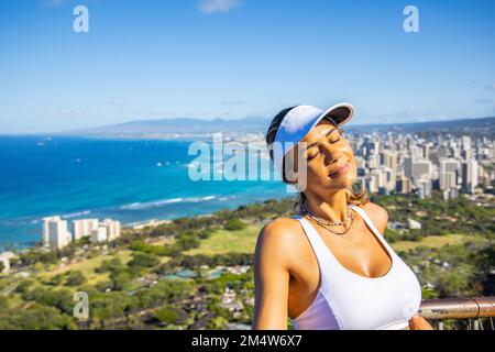 Porträt einer jungen Weißen, die ihren Urlaub auf der Insel O'ahu, Hawaii, mit der Stadt Honolulu im Hintergrund genießt Stockfoto