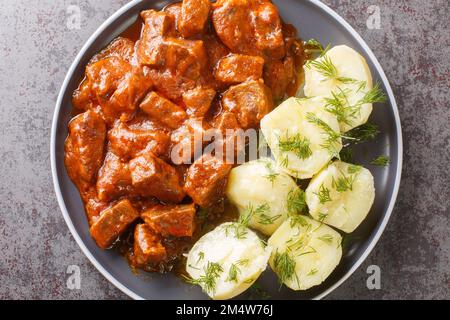 Wiener Saftgulasch ist ein herzhafter Eintopf, der aus gewürfeltem magerem Rindfleisch besteht, getränkt in einer dicken, aromatischen Soße auf dem Teller auf dem Tisch. Horizontal Stockfoto