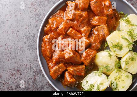 Österreichisches Rindergulasch in einer dicken, reichen Sauce mit gekochten Kartoffeln, Nahaufnahme auf einem Teller auf dem Tisch. Horizontale Draufsicht von oben Stockfoto