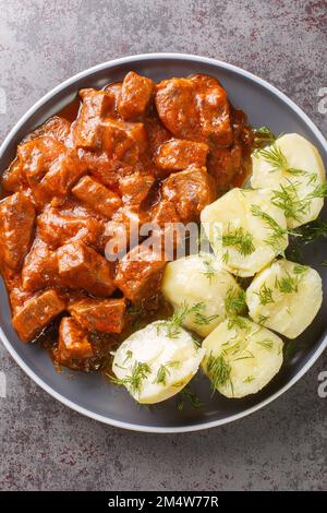 Authentisches österreichisches Rindfleisch Gulasch, das für seine besonders dicke Soße auf dem Teller auf dem Tisch bekannt ist. Vertikale Draufsicht von oben Stockfoto