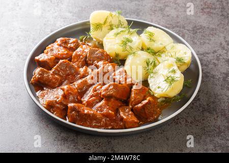 Wiener Rindergulasch mit dicker Sauce, serviert mit gekochten Kartoffeln, Nahaufnahme auf einem Teller auf dem Tisch. Horizontal Stockfoto