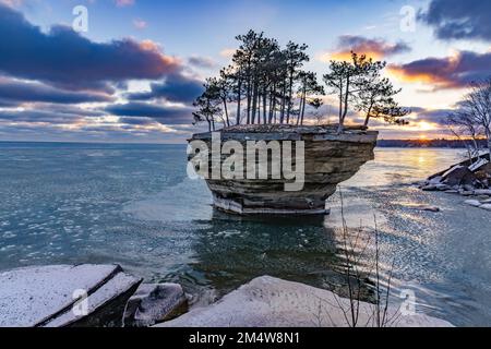 Der Sonnenaufgang am Turnip Rock an der Spitze von Michigans Daumenspitze in der Nähe von Port Austin wird im frühen Winter gezeigt. Pfannkucheneis schwimmt auf der Oberfläche des Lake Huron Stockfoto