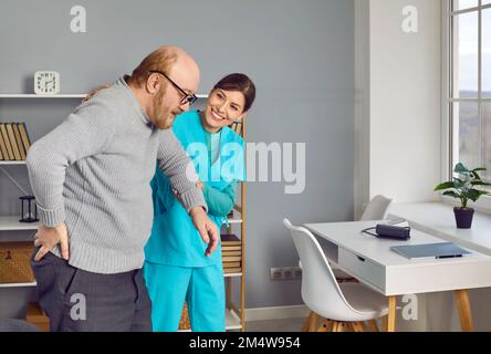 Eine lächelnde Krankenschwester, die einem pensionierten älteren Mann beim Gehen hilft, seine Hand hält, ihn unterstützt Stockfoto