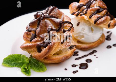 Kuchen mit Schokolade und Eis, auf weißem Teller, auf schwarzem Hintergrund Stockfoto