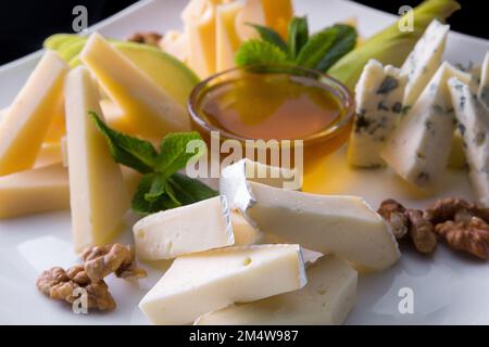 Gemischter Käse mit Nüssen und Honig auf einem weißen Teller Stockfoto