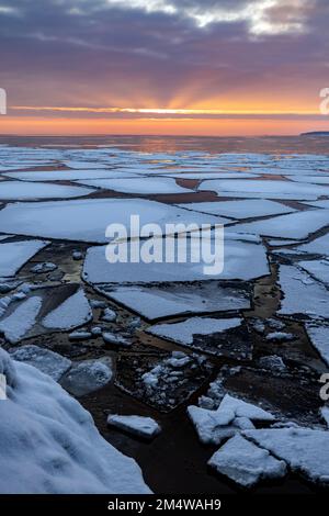 Eisschollen schwimmen auf der Oberfläche des Lake Superior unter einem wunderschönen Sonnenaufgang, wenn der Tag bricht und die Winterpause beginnt. Stockfoto