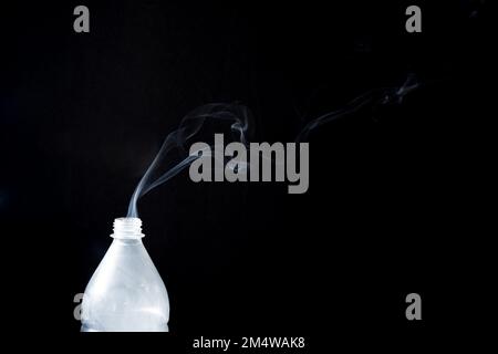 Der Rauch aus einer Plastikflasche auf schwarzem Hintergrund - Aromatherapie-Konzept Stockfoto