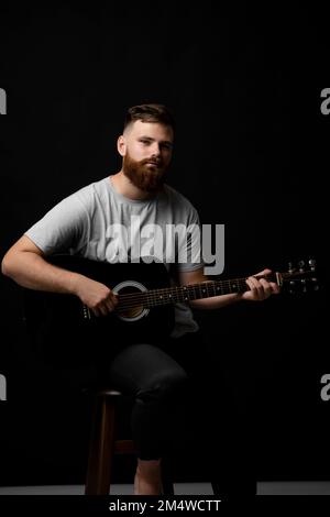 Portarait eines bärtigen Musikers, der in einem dunklen Raum Akustikgitarre spielt. Stockfoto