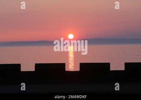 Isle of Arran, Schottland, Großbritannien. Sonnenuntergang über der Insel vom Strand in Ayr. Bekannt als der schlafende Riese aufgrund seines Umrisses, besonders von der Ayrshire Coast aus gesehen. Sonnenuntergang im Firrth von Clyde. Stockfoto