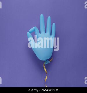 Medizinische Handschuhe aus blauem Latex als Ballon auf violettem Hintergrund, zeigt den Charakter in Ordnung. Farbig in sehr peripher - Farbe des Jahres 2022. Minimalismuskonzept. Stockfoto