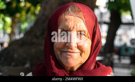 Porträt einer alten muslimischen Frau, die roten Hijab trägt. Alte Frau, die lächelt und in die Kamera schaut Stockfoto