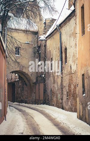 Wunderschöne enge Straße in der Altstadt von Vilnius, alte Gebäude und Straßenlaternen im Winter bedeckt von Schnee und Eis, vertikal Stockfoto