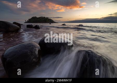 Wellen beben und fließen um die Felsen der Küste, während die Sonne über dem Lake Superior im Little Presque Isle Park nahe Marquette Michigan, USA, aufgeht Stockfoto