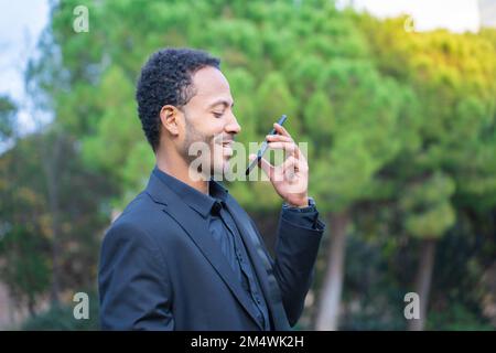 Nahaufnahme eines attraktiven jungen afroamerikanischen Mannes, der im Freien mit einem Mobiltelefon spricht Stockfoto