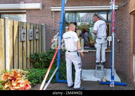 Urk, Niederlande - 28. August 2019: Maler, die einen Hausfensterrahmen für die Neumalerei vorbereiten Stockfoto