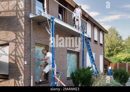 Urk, Niederlande - 28. August 2019: Zwei Maler, die mit der Entfernung alter Farbe und der Vorbereitung eines Fensterrahmens für die Neumalerei beschäftigt sind Stockfoto