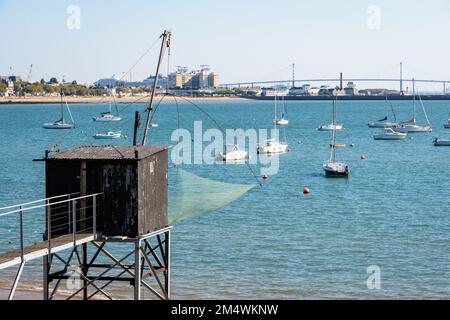 An einem sonnigen Sommertag steht eine hölzerne Angelkabine mit einem großen quadratischen Aufzugsnetz namens „carrelet“ am Strand gegenüber der Saint-Nazaire-Brücke. Stockfoto