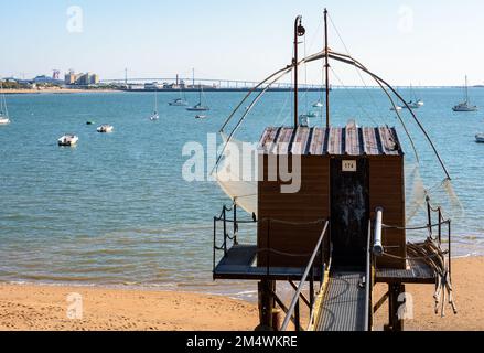 An einem sonnigen Sommertag steht eine hölzerne Angelkabine mit einem großen quadratischen Aufzugsnetz namens „carrelet“ am Strand gegenüber der Saint-Nazaire-Brücke. Stockfoto