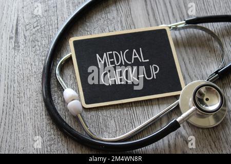 Stethoskop und Kreidetafel mit Text-VORSORGEUNTERSUCHUNG auf Holztisch. Medizin- und Gesundheitskonzept Stockfoto