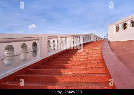 Rote, sonnenbeleuchtete Treppen und weiße Geländer am blauen Himmel. Konzept, Aufstieg Stockfoto