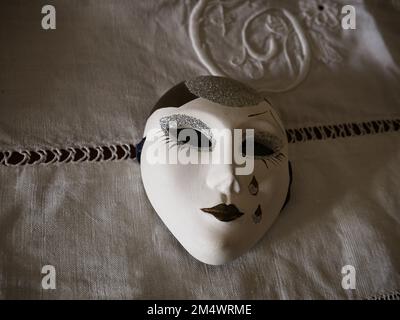 Kleine handbemalte venezianische Maske auf einer Tischdecke aus den frühen 1900er - Venedig - Italien Stockfoto