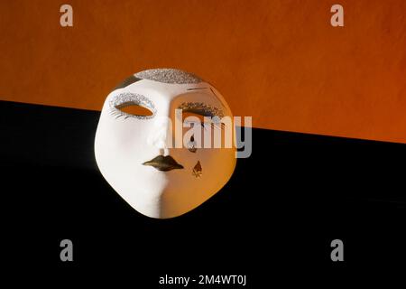 Kleine venezianische Maske Hand gemalt auf einem orange-schwarzen Hintergrund - Venedig - Italien Stockfoto