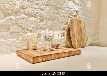 Ein Holzbrett auf einem weißen Tisch neben einer Vase mit Blumen und einem leeren Glas Stockfoto