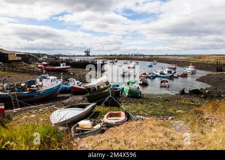 Boote liegen im Hafen an Paddys Hole, Redcar, England, UK mit industriellem Teesport im Hintergrund Stockfoto