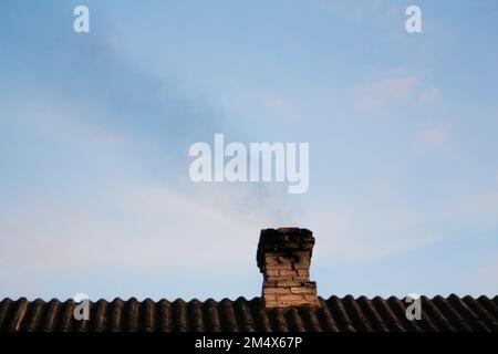 Unschärfe-Rauch aus dem Kamin eines Hauses, das mit Kohle betrieben wird. Schwarzer Rauch aus dem Kamin eines Apartmentgebäudes während der Heizung auf dem Ro Stockfoto