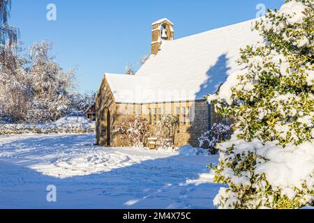 Frühwinterschnee auf der kleinen Steinkirche St. Mary in Hamlet (erbaut 1958) im Dorf Cotswold Birdlip, Gloucestershire, England Stockfoto