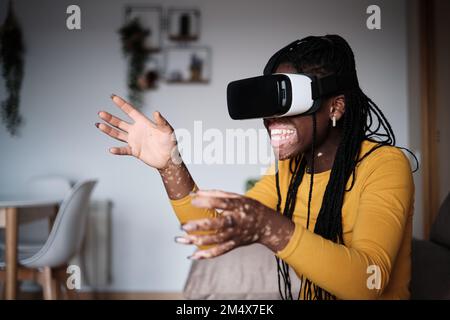 Fröhliche schwarze Frau mit Vitiligo-Haut, die Videospiele in VR spielt Stockfoto