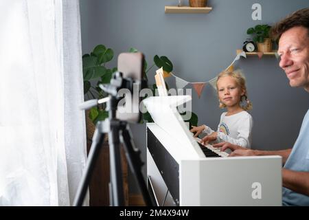 Vater und Tochter lernen zu Hause Klavier über das Mobiltelefon zu spielen Stockfoto