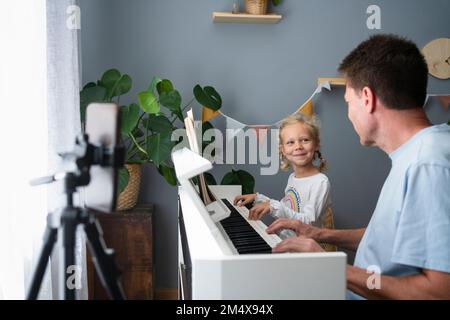 Lächelndes Mädchen, das mit Vater zu Hause Klavier spielt Stockfoto