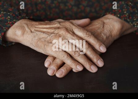 Seniorin mit zerknitterten Händen auf dem Tisch Stockfoto