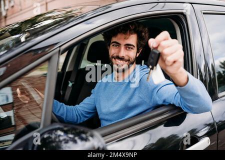 Ein lächelnder Mann, der im Auto sitzt und den Schlüssel hält Stockfoto